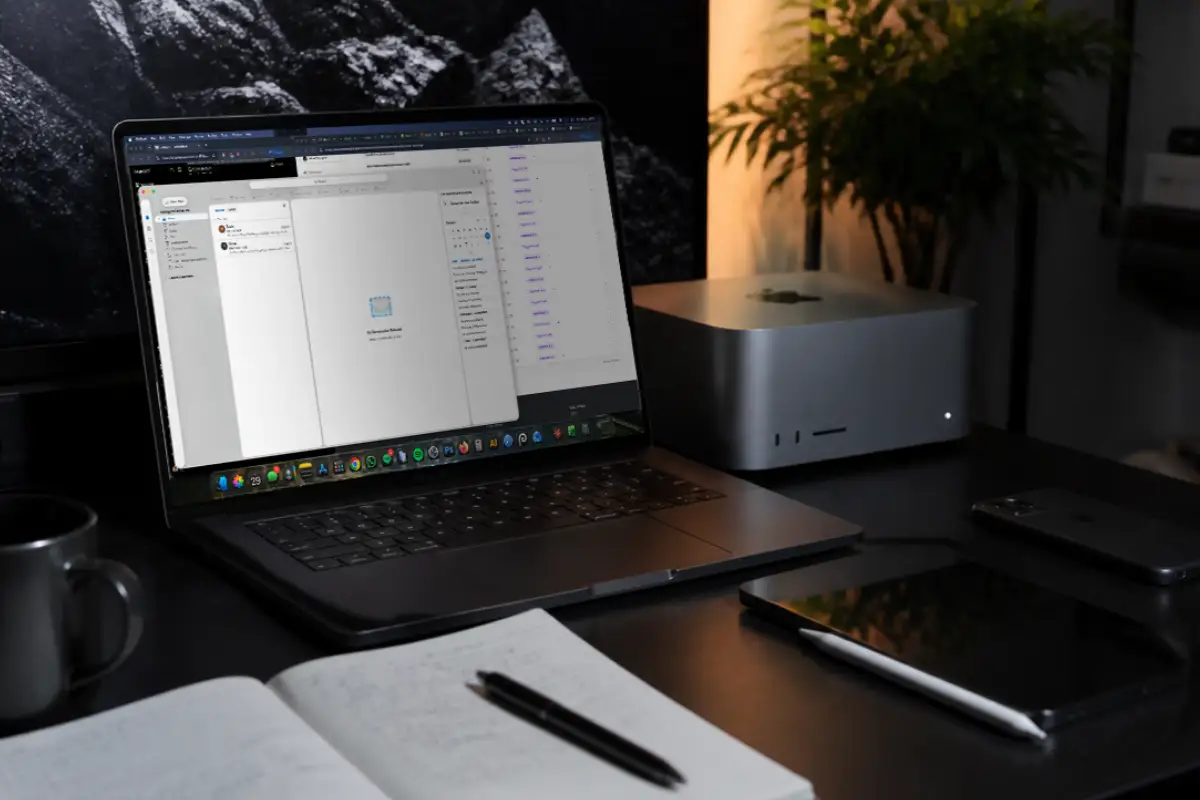 Web design workspace with a laptop open to email and project management tools, alongside a notebook, tablet and desktop computer
